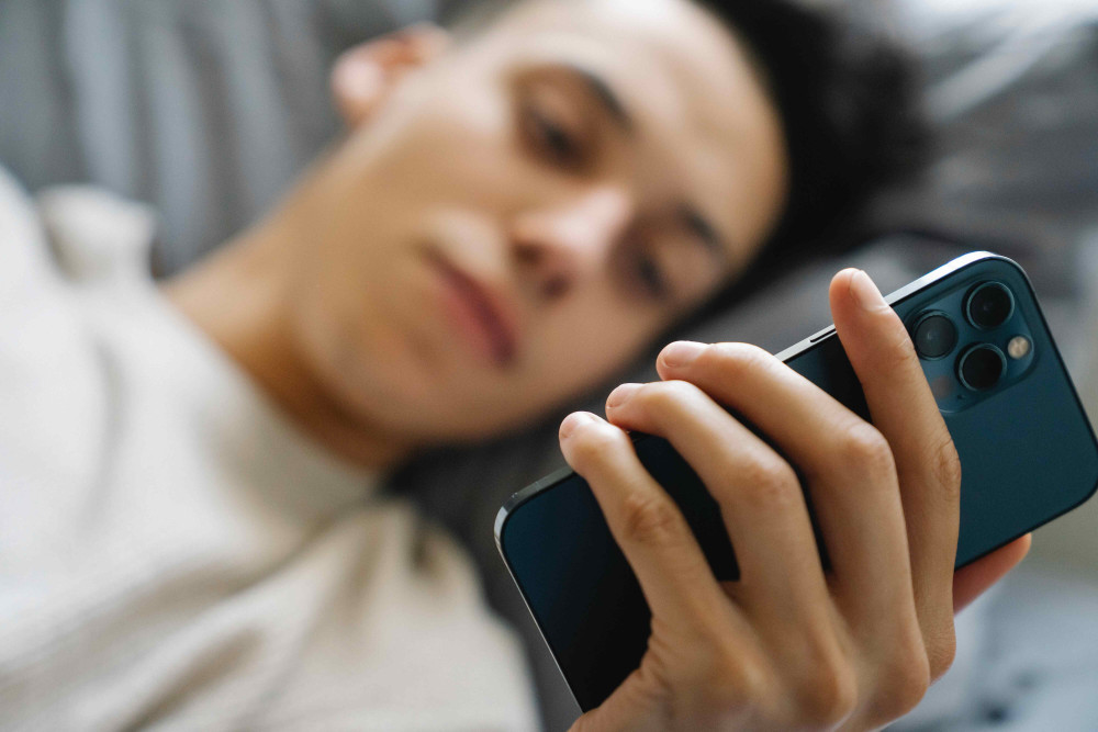 Teenager liegt auf dem Bett und hat den Blick auf sein Smartphone gerichtet